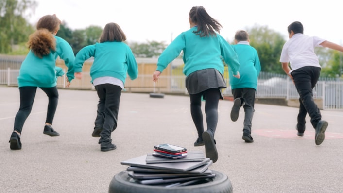 DisconnectToReconnectA: Image shows pupils running away from a pile of devices in a playground.