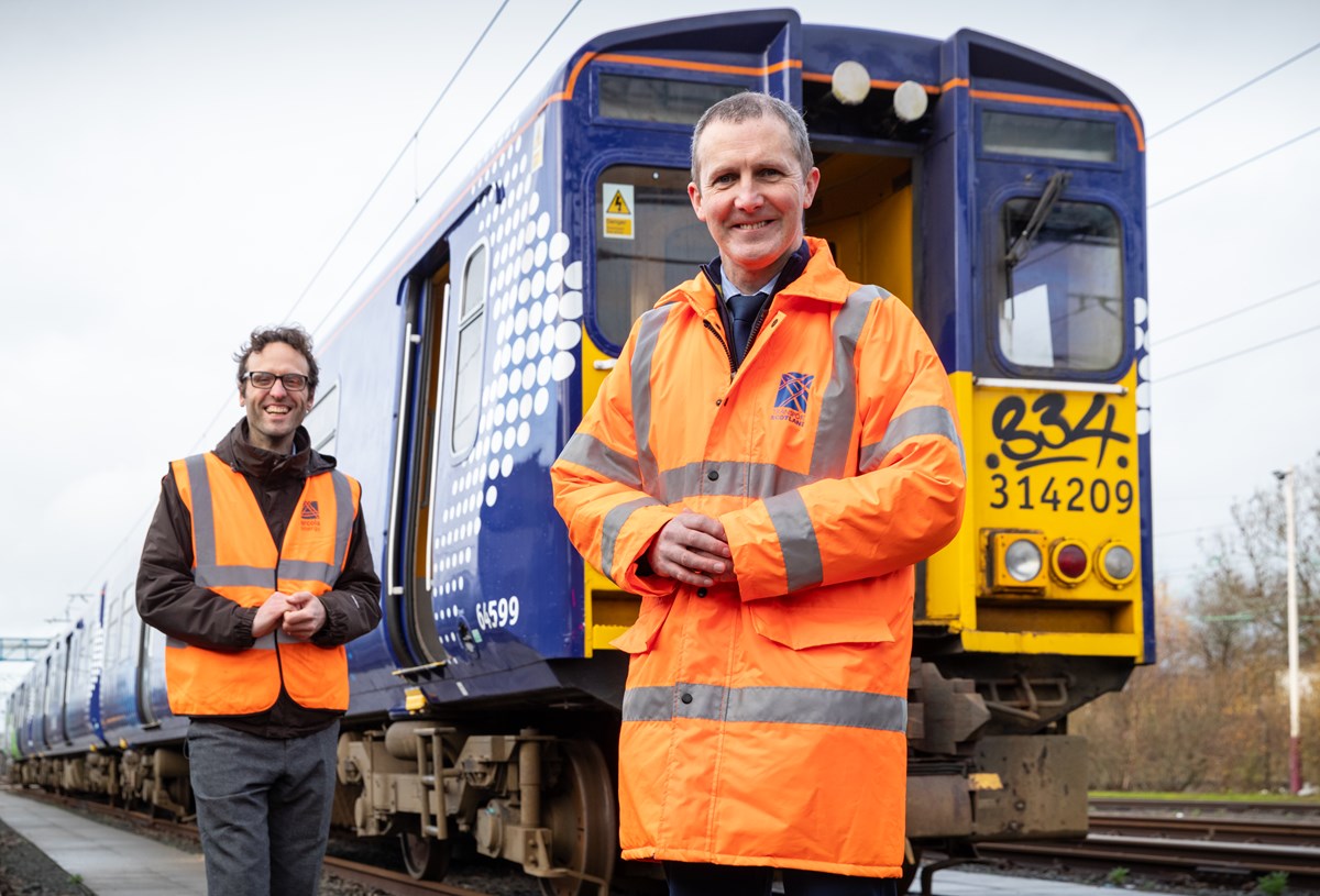 Image shows, Michael Matheson MSP - Cabinet Secretary for Transport, Infrastructure and Connectivity (orange jacket) photographed with Dr. Ben Todd, CEO of Arcola Energy (hi-viz waistcoat) and a 314 Class electric train at the Scotrail Depot in Yoker, Glasgow