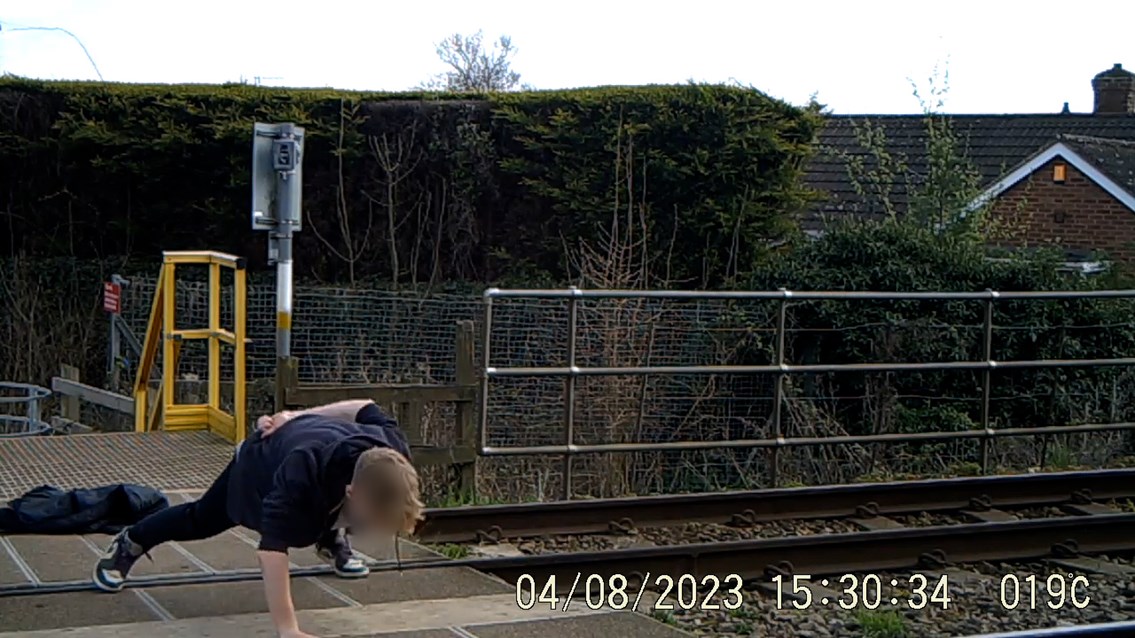 Youth doing on armed press ups on level crossing while listening to loud music