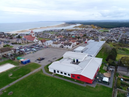 Aerial view of St Gerardine Primary School, featuring its red and white buildings. The scenic coastline and sandy beach can be seen in the background.