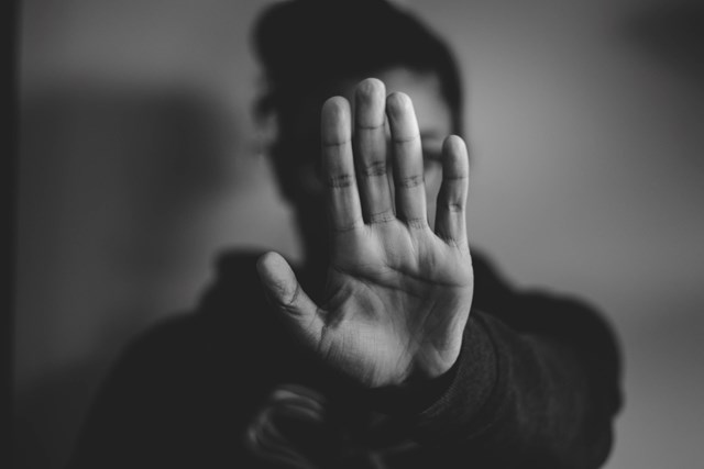 Domestic Abuse Strategy image - Dec 19: A black and white photograph of a woman holding her hand out in front of her. The palm of her hand is in focus and obscuring her face. The woman is in the background out of focus.