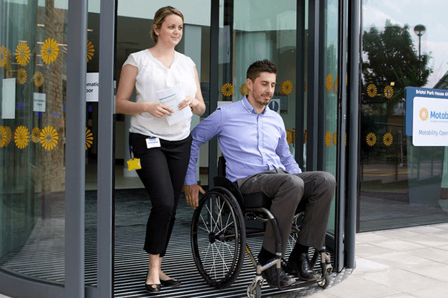 Motability Operations half year report image: Woman holding papers exits Motability Operations office next to man in wheelchair