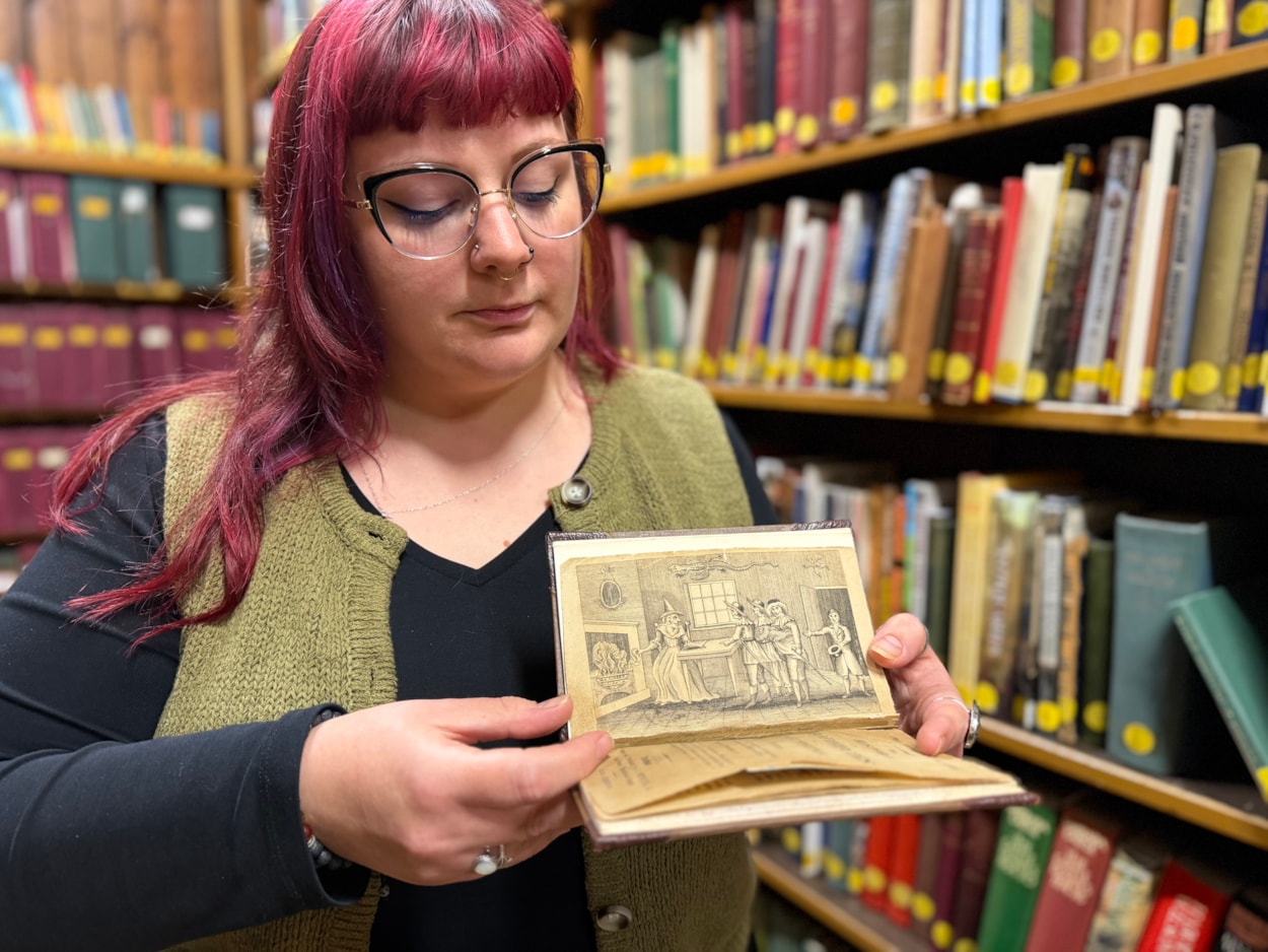 Mother Shipton book: Librarian Sally Hughes with a vivid woodcut illustration that depicts a famous scene when the soothsayer Mother Shipton was reputedly confronted by nobles sent to her cottage by the powerful Cardinal Wolsey, who was furious she had made the treasonous prediction that he would never set foot inside the city of York.
Under threat of being burned at the stake, a defiant Mother Shipton was said to have plucked a handkerchief from her head and thrown it into the fire, proclaiming that if it did not burn, then neither would she.