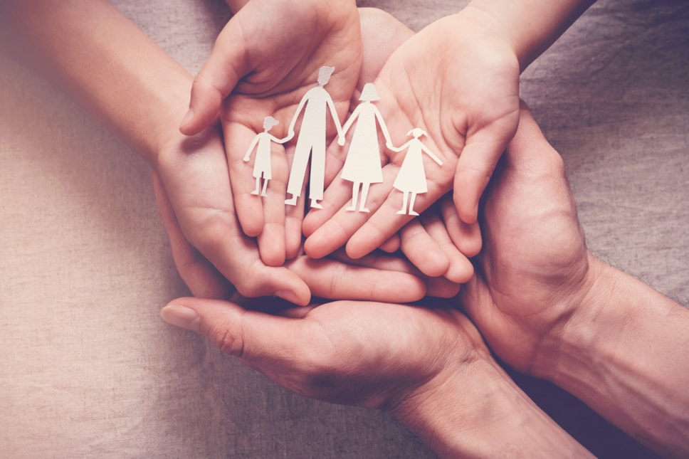 Cut outs of a family of four placed in the hands of two adults and a child all on top of one another.