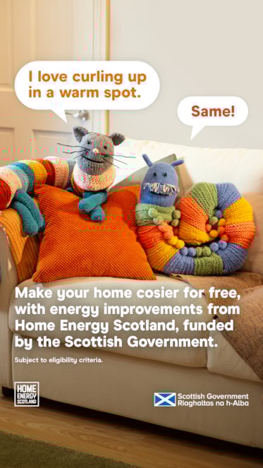 Knitted cat and snake with speech bubbles saying 'I love curling up in a warm spot' and 'Same!' on a couch. Text promotes free energy improvements from Home Energy Scotland, funded by the Scottish Government. Logos and eligibility note included.