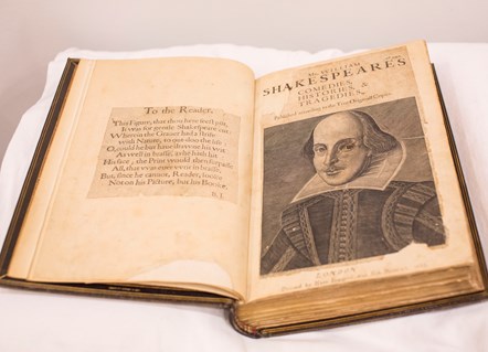 The First Folio rests on a pillow and is open at the title page, showing a portrait of Shakespeare.