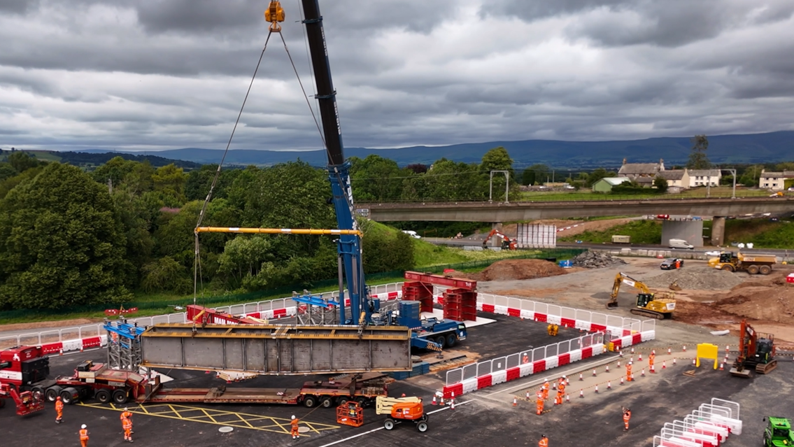 Huge steel beams arrive for railway bridge renewal over M6 in Penrith: A still of a steel section being lifted onto tressels