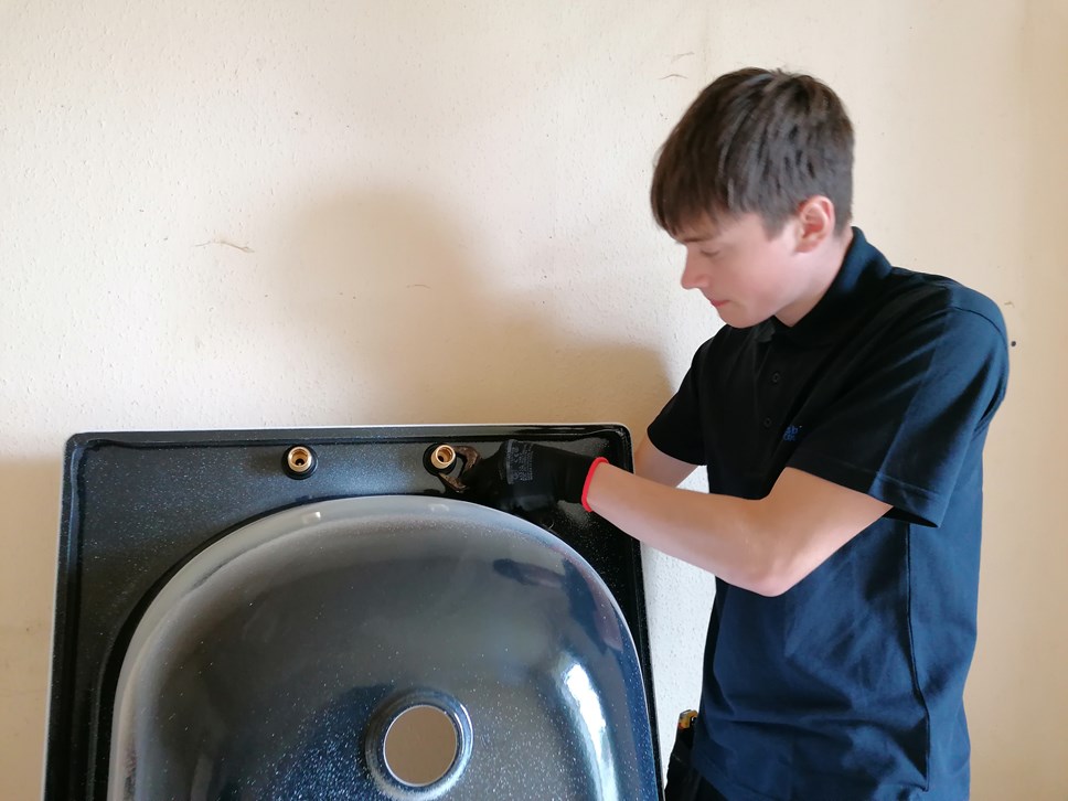 Modern Apprentice Plumber Logan Chilton works on a bath installation using a wrench