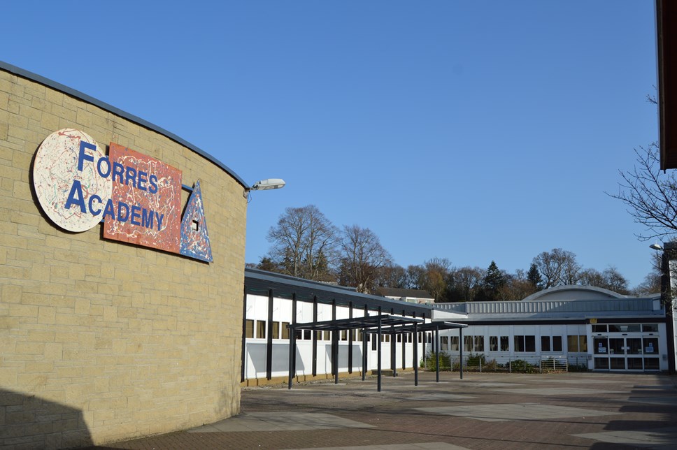 An exterior photograph of Forres Academy with a big expanse of deep blue sky and some bare beech trees in the distance.