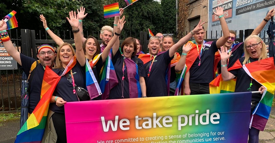 Colleagues ready for the Manchester Pride parade: a group of people holding rainbow banners and flags