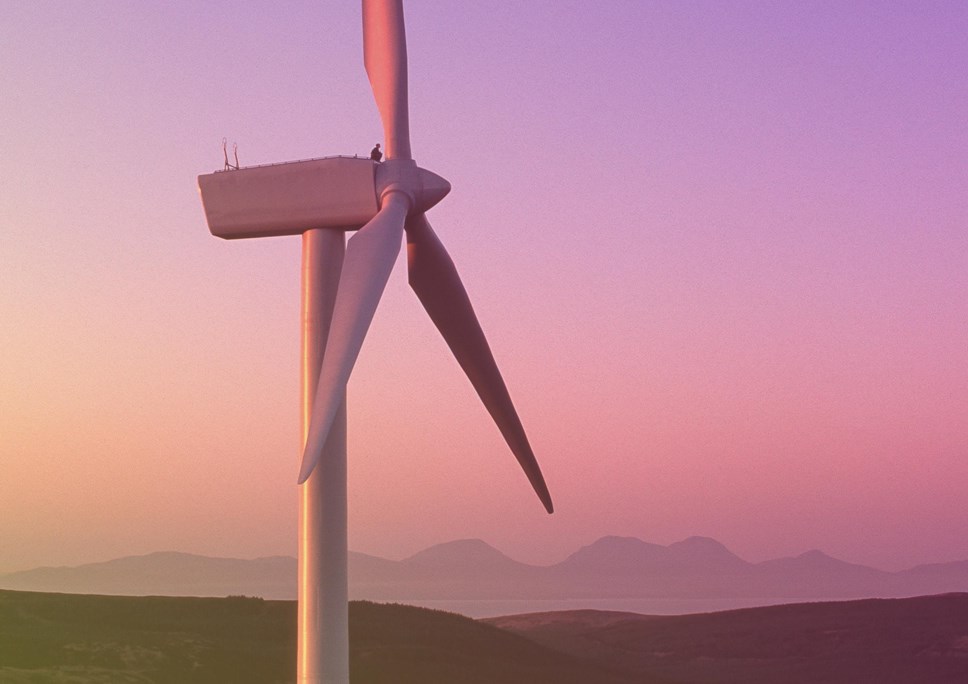 man sitting on top of a wind turbine turned pink by the setting sun; Isle of Jura in the background Large Image m21562