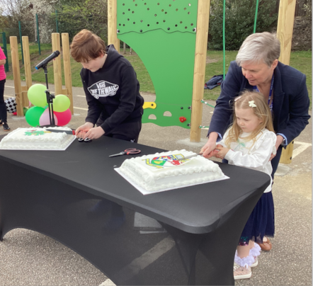 Head teachers and pupils cutting a celeberation cake at a school playground opening event.