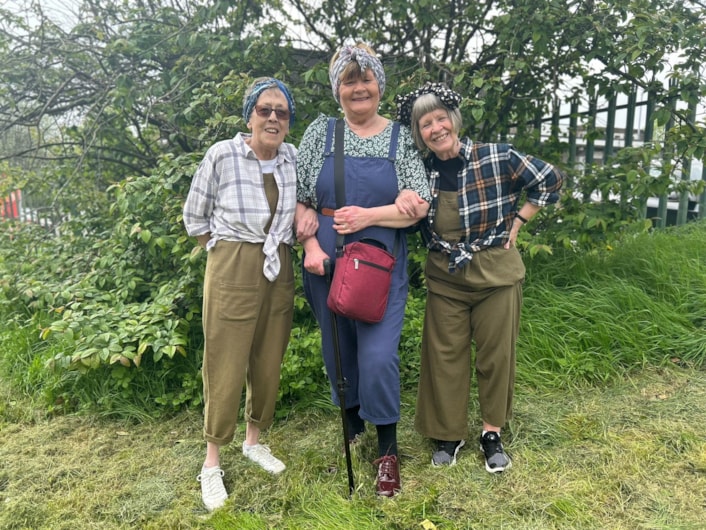 Burmantofts Community Friends members dress up in Land Army uniforms - D Day event: Three women dressed in dungarees and shorts, with scarves on their heads, linking arms.