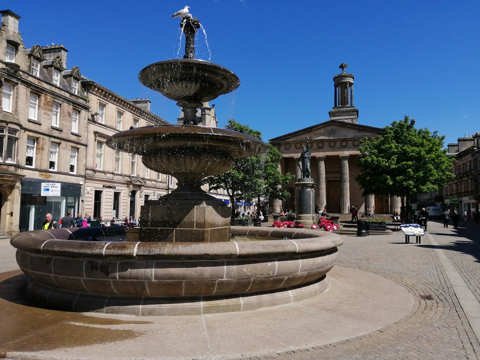 A cobbled town centre with autumnal trees is lined by buildings on either side with a large church with columns in the front in the middle.