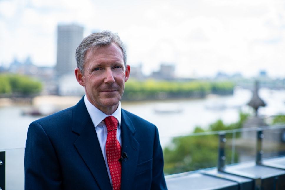 A man in a suit looking at the camera, with a blurry background