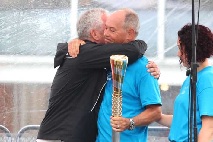 Baton of Hope tour 1-2: Steve is holding the baton of hope, wearing a blue Baton of Hope t-shirt, hugging Mike McCarthy