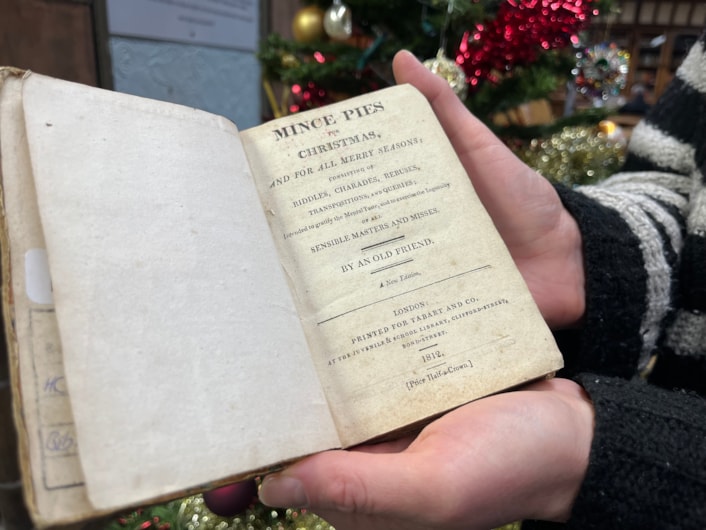 Library Christmas books: Library and digital assistant Anna Jones with a book of children’s Christmas games from 1812 entitled Mince Pies for Christmas. Filled with riddles and games, the book claims ‘to exercise the ingenuity of all sensible masters and misses.’
Some of the charades within its pages have been circled by the children who must have  played the game with their families at Christmas more than 200 years ago.