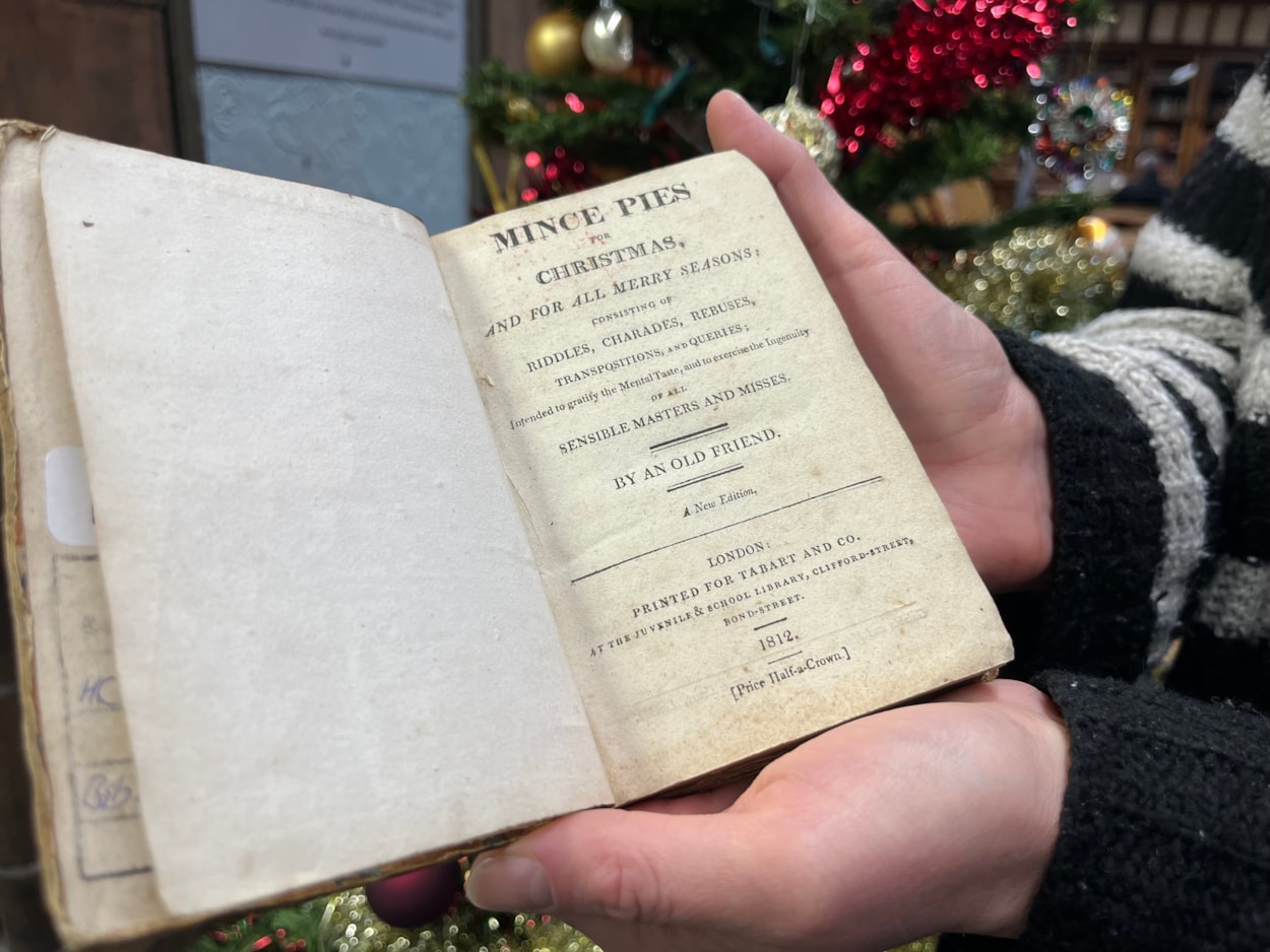 Library Christmas books: Library and digital assistant Anna Jones with a book of children’s Christmas games from 1812 entitled Mince Pies for Christmas. Filled with riddles and games, the book claims ‘to exercise the ingenuity of all sensible masters and misses.’
Some of the charades within its pages have been circled by the children who must have  played the game with their families at Christmas more than 200 years ago.