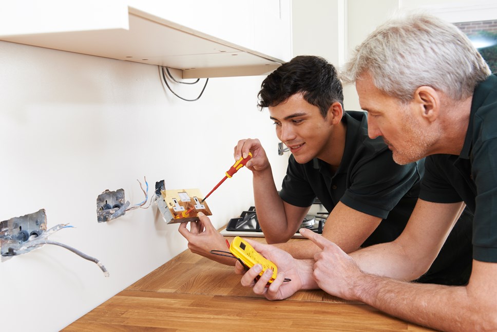 apprentice electrician with mentor in kitchen wiring a socket