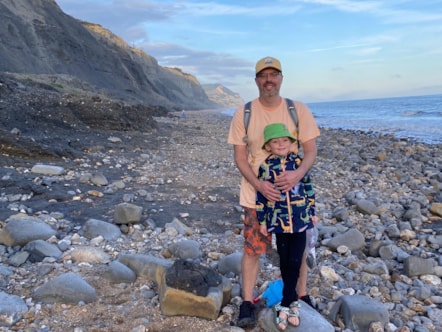 Man and boy stand on pebbled beach.