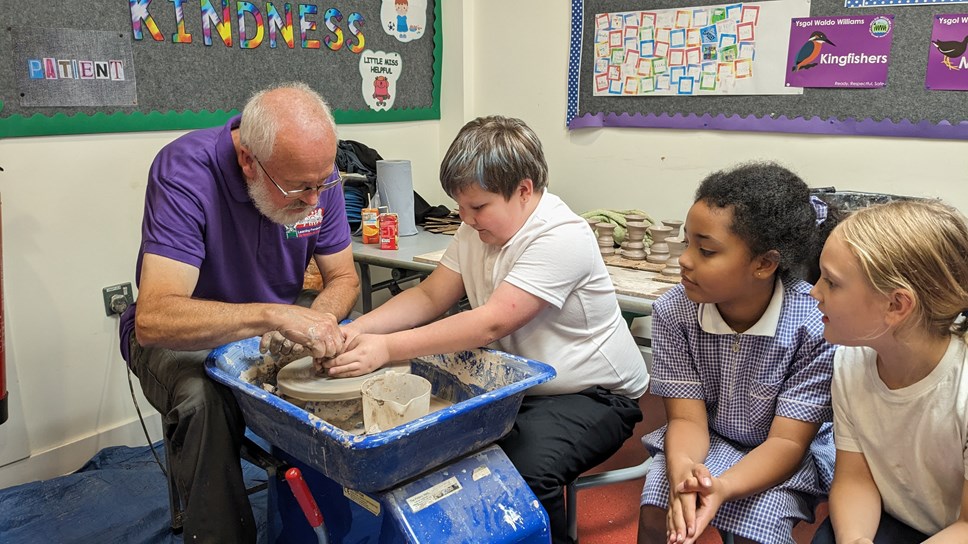 Three children learning how to use pottery wheel from grey haired man