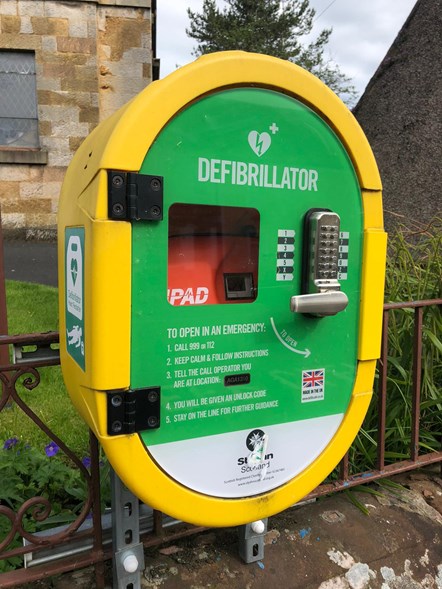 Community defibrillator box attached to wall and railings in Stewarton
