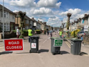 PlayStreet RoadClosure: Residential road blocked off by wheelie bins, signs attached to the bins read 'road ahead closed' and 'road open for play'