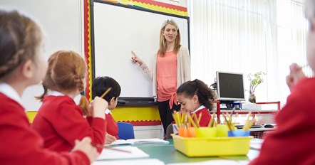 Teacher pointing at board in a primary school class.