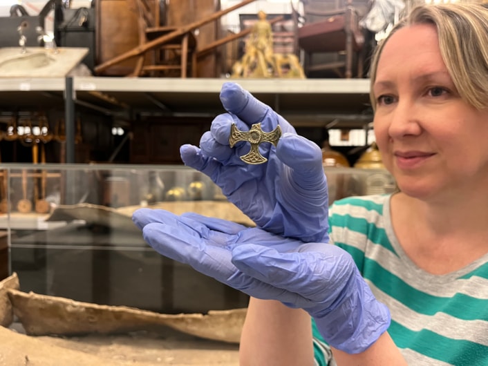Saxon cross: Kat Baxter, Leeds Museums and Galleries' curator of archaeology with the Saxon pendant.
Believed to date from the eighth century, the gilded pectoral cross may have once been a badge of office for an important church leader or official and was unearthed last year by a metal detectorist.
With one arm broken, and the central stone now missing, the cross is nevertheless a stunning example of metalwork, made from solid silver covered with a thin layer of gold leaf.
In the background is a lead coffin which was buried for more than 1,600 years before it was discovered in a previously unknown cemetery site near Garforth alongside the remains of more than 60 individuals from late Roman to early Saxon periods.