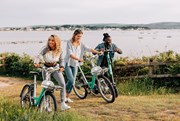 Beryl-BCP-2: Three riders pushing their Beryl vehicles up a grass verge. The rider on the right is a young male pushing an e-scooter and the other two are young females pushing bikes.