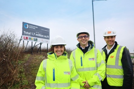 The three people in the photo caption are stood together wearing hard hats and high viz jackets, with the sign in the background.