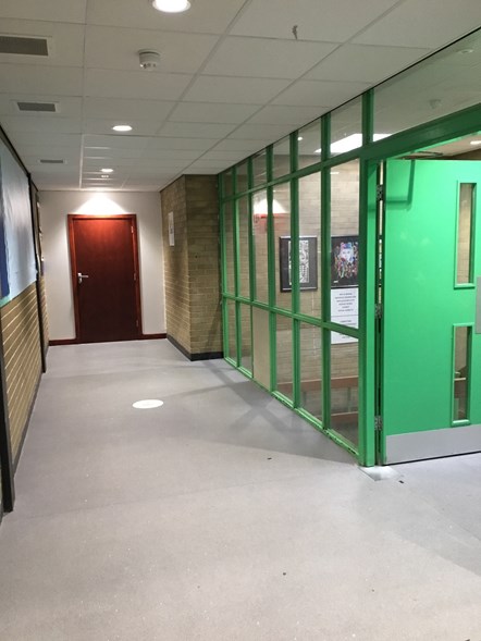 Corridor surrounded by brick walls. There's an entry to a staircase on the right that is painted green and a door at end of the corridor.
