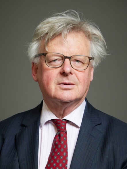 Colour head shots of Cumbrian peer Lord Inglewood who is wearing glasses and wearing a dark blue jacket, striped shirt and red patterned tie