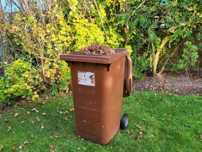 Brown bin longshot - landscape: Image showing brown bin in garden filled with garden waste