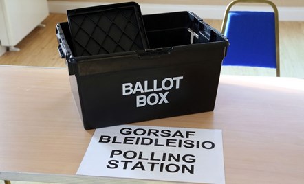 A Ballot Box on a table with the words polling station written in English and Welsh.