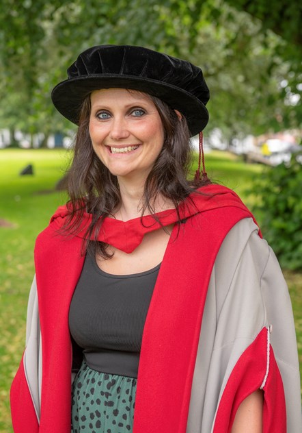 Female academic dressed in silver grey and red academic robes and black bonnet style cap