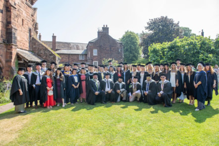 A large group of University of Cumbria graduates in academic caps and gowns in the grounds of Carlisle Cathedral