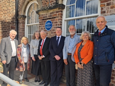 Group of eight people stood under new blue plaque at the University of Cumbria