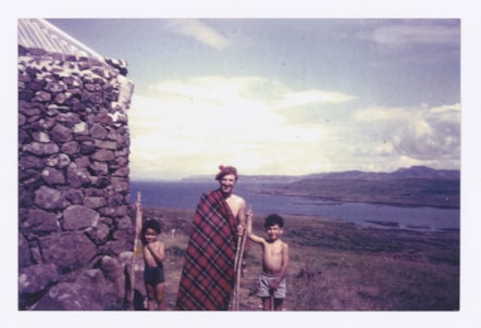 On a family holiday in Mull, Jackie Kay's dad stands wrapped in tartan, holding a wooden stick like a staff. To his left, a young Jackie Kay stands with a staff of her own. To his left, her brother Maxie also stands holding a staff.