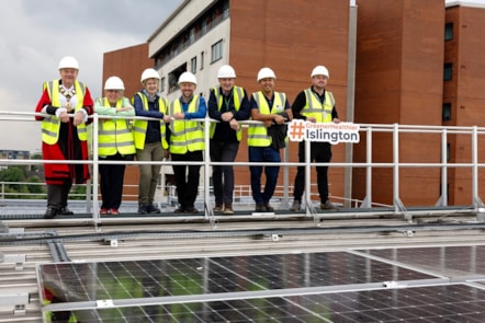 A group picture on the roof of Islington's Waste and Recycling Centre, showing new solar panels. A sign is being held up, reading #GreenerHealthierIslington