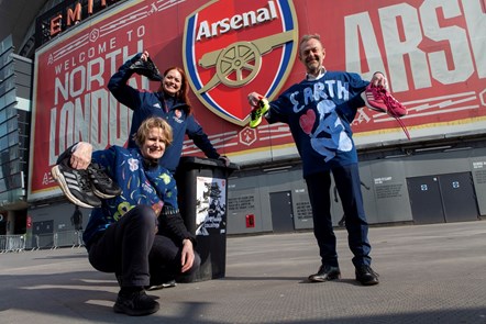 Cllr Champion, Helen Staniland from Arsenal in the Community, and Keith Townsend pose next to the boot collection bin, wearing upcycled t-shirts donated by Arsenal