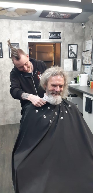 Danny sits in a barbers chair as his beard is cut