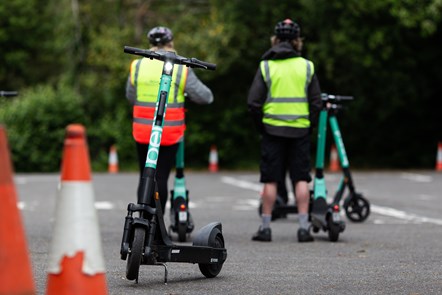 Users taking part in e-scooter training with a licensed instructor in Bournemouth. There is a parked e-scooter and two traffic cones in the foreground of the picture.