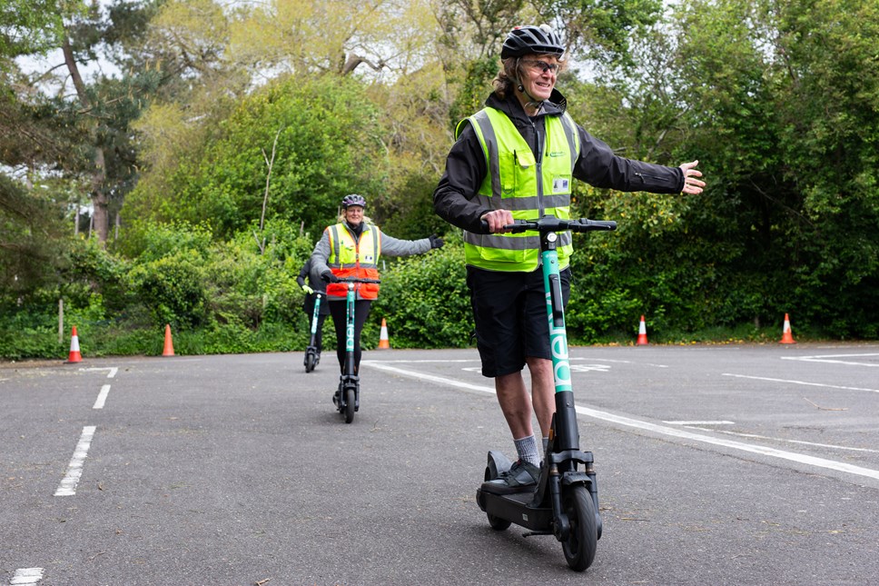 A licensed instructor taking part in an e-scooter safety training course in Bournemouth. The trainer is leading two other riders and using his left arm to indicate.