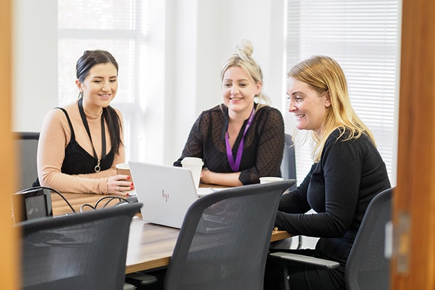 Motability Operations Achieves Disability Confident Leader Status: Three women sit at table in boardroom looking at a laptop placed on table in front of them