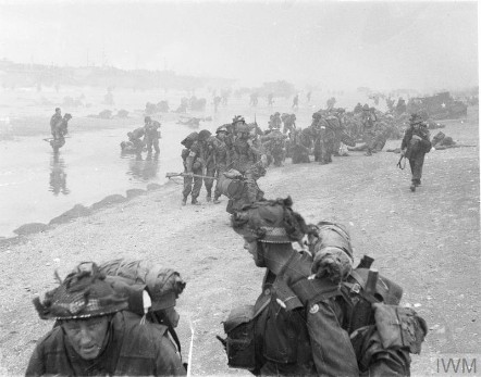 Soldiers in a snaked line clamber up a beach in WWII.