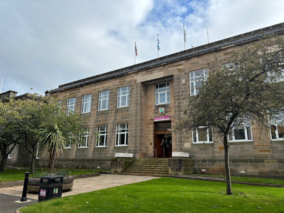 The image shows Moray Council HQ, a stone building with large windows, a central entrance and flags on the roof.