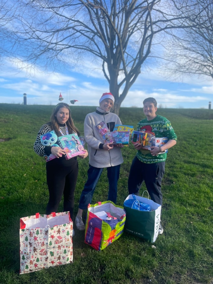 CFL Christmas appeal 4: Three people are shown in Christmas outfits holding armfuls of toys in a field.