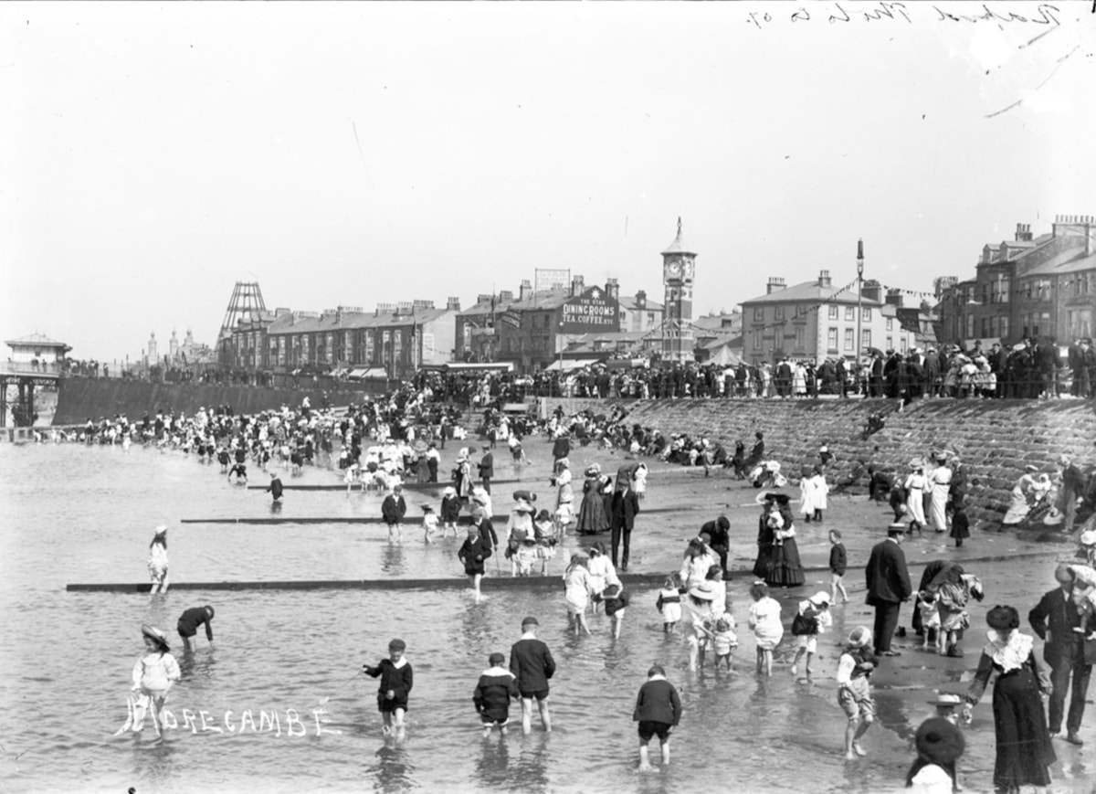 The clock tower, a gift to the town of Morecambe in 1905 by Councillor John Robert Birkett, who was Mayor of Morecambe nine times. The skeleton of Morecambe Tower is on the left, which was was removed around the time of the Great War,  with only the complex around the base surviving until 1961.  On the far left is the entrance to the (Central) Pier, which opened in 1869. It boasted a pavillion known as the 