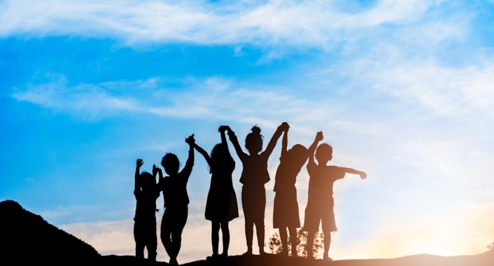 Foster Carer Fortnight: Image shows a group of children holding hands in the air, against a blue sky.